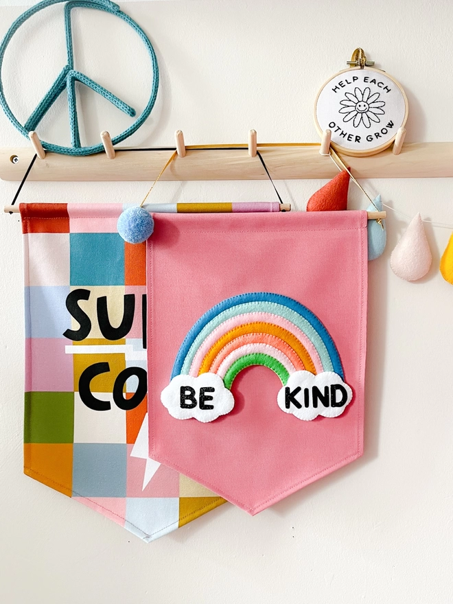 Pink be kind banner hanging from a wooden peg rail