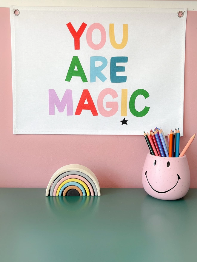 You are magic wall banner in rainbow colour palette hanging on a pink wall