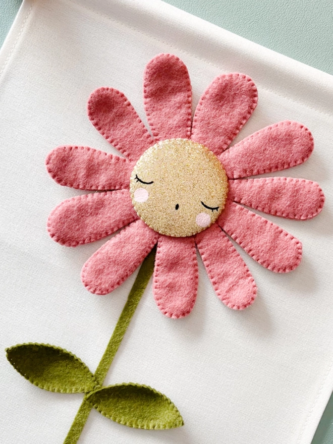 A pink Daisy with a gold sleepy painted face on a white background