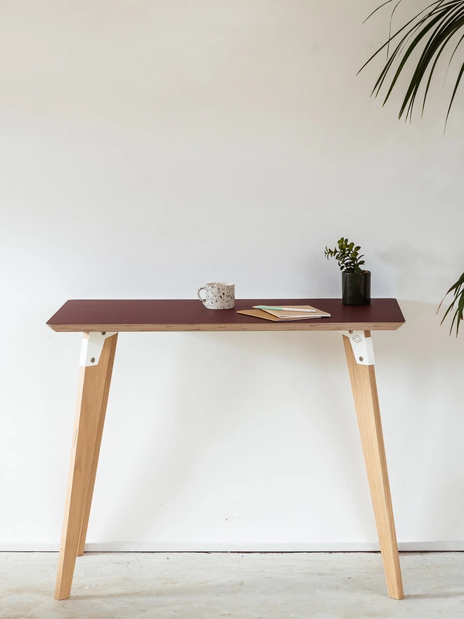 A stylish and minimalist standing height desk with burgundy Fenix top, white coloured steel brackets and solid oak legs.