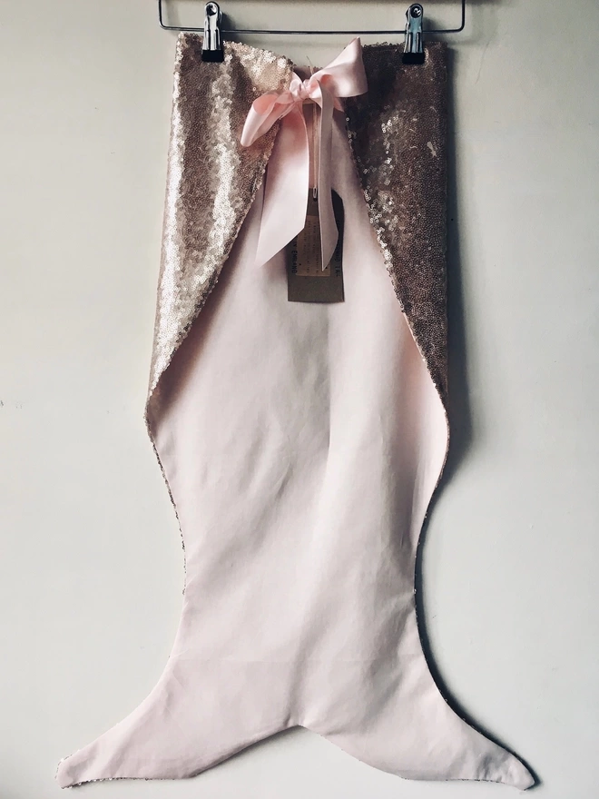 Front view of a pink sequin mermaid tail on a hanger, a large pink ribbon bow at the waist