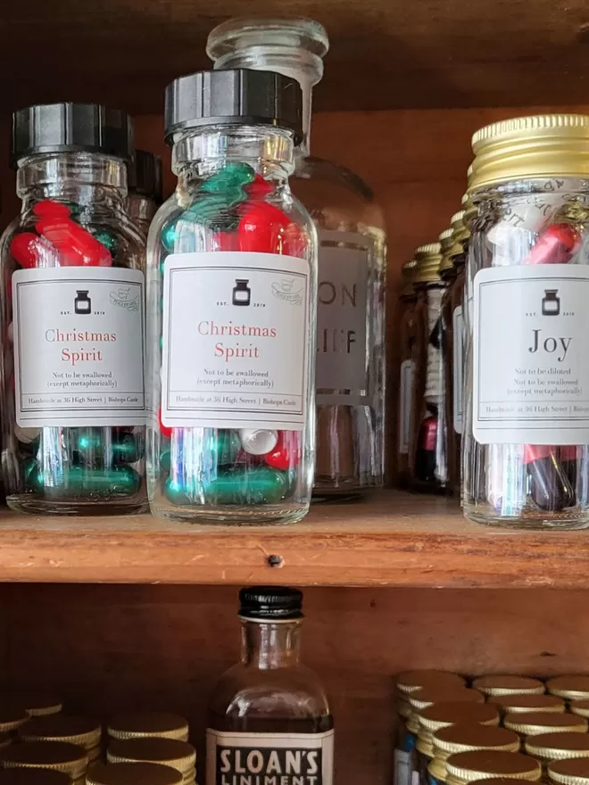 Glass bottles on Pharmacy shelves containing red and green Christmas Spirit poetry pills 