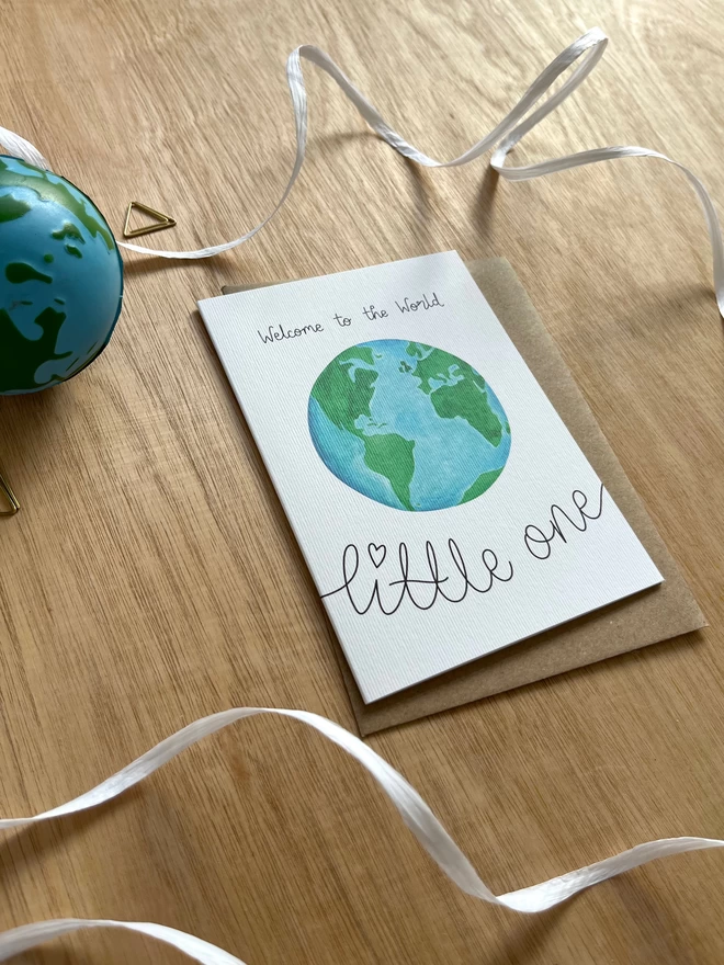 a greetings card featuring an illustration of the earth surrounded by the phrase “welcome to the world little one”