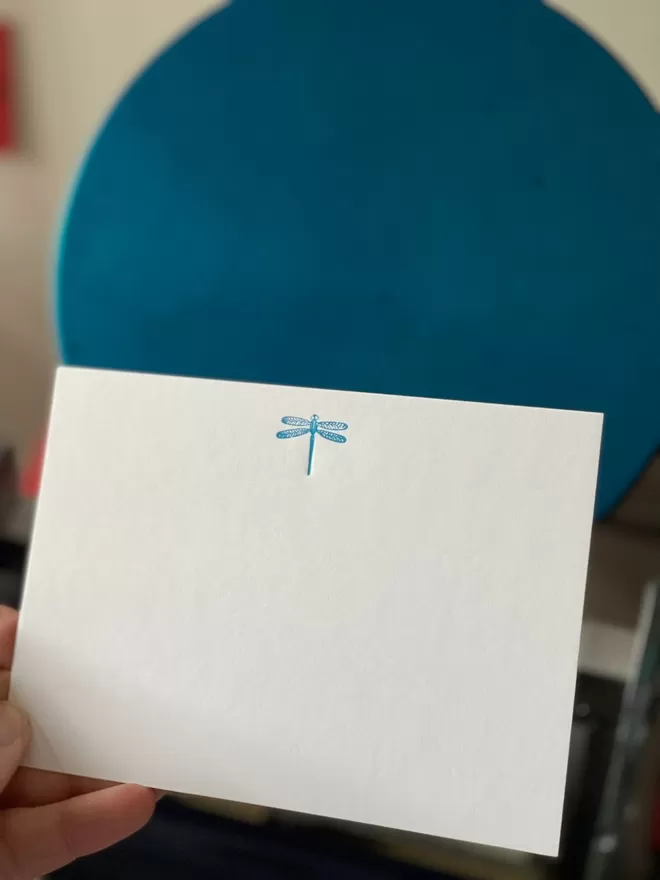 South London Letterpress Dragonfly Notecard seen held up in front of a blue chair.