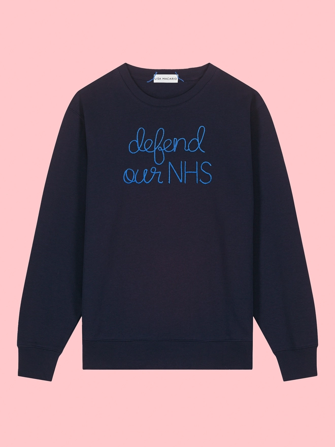 A black sweatshirt embroidered with defend our NHS on a pink background