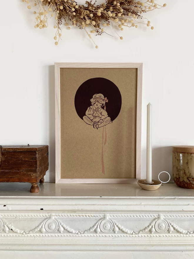 A4 art poster print of serene praying girl sat cross legged with hair bow in maroon circle printed on kraft card in pale pink frame