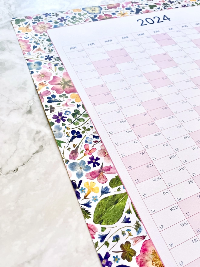 Angled View - 2024 Wall Planner with Floral Border on Stone Marble Worktop
