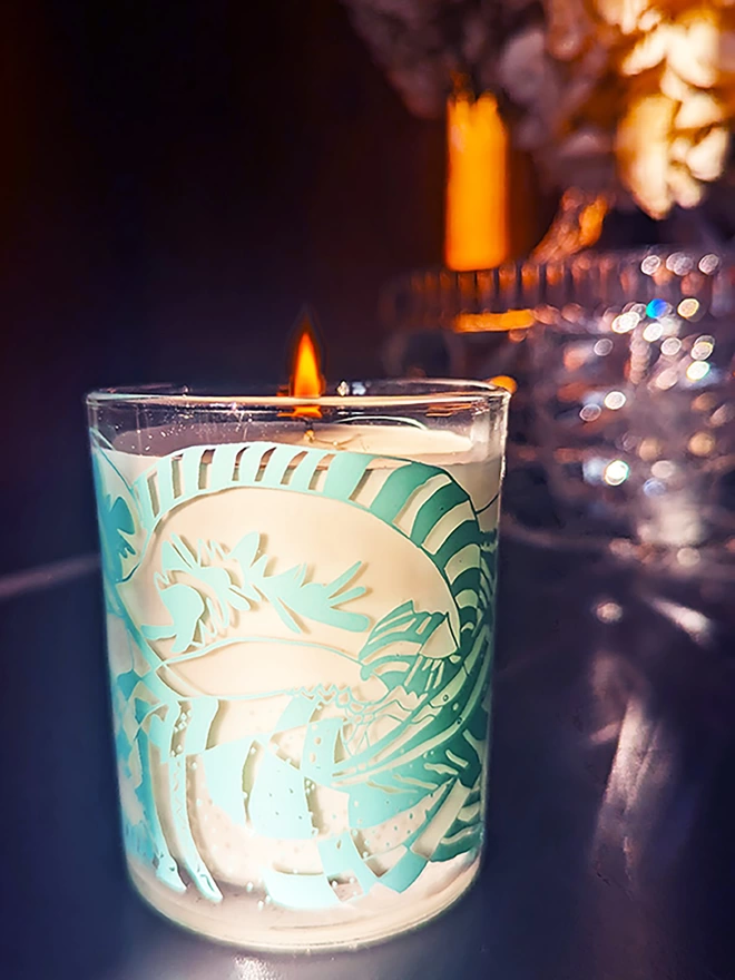 the wave black pomegranate charity candle in a reusable glass with light blue illustrations