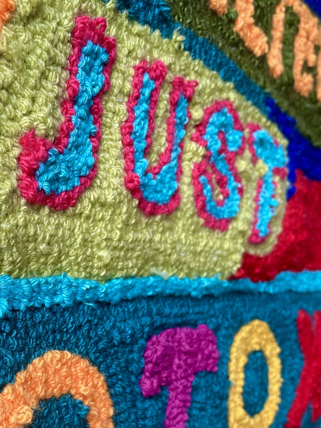 "Just" in bluepunch needle wool art with a pink edging on a lime green background