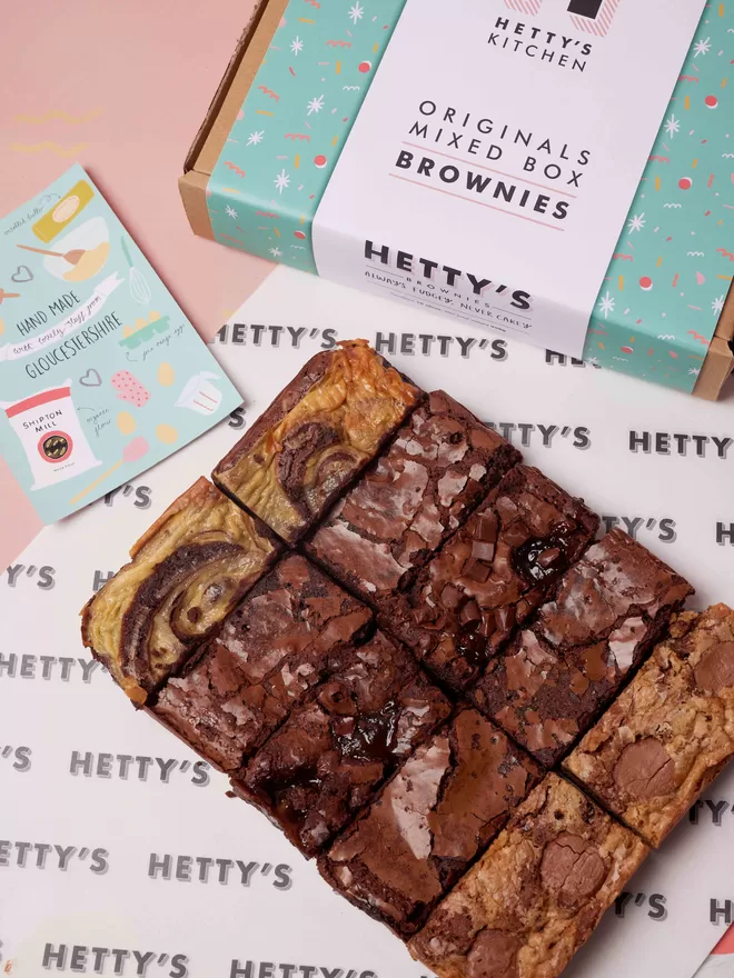 Ten slices of Hetty's brownie original flavours of marbled cheesecake, salted caramel, classic fudge, cookie dough and chocolate orange in a flat lay with branded box and postcard