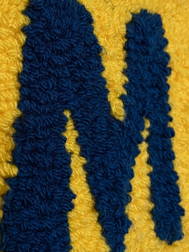 Close up of woollen "M" in navy wool on yellow background