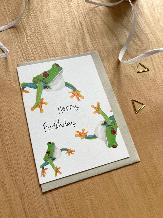 a greetings card featuring three green tree frogs with the phrase “hoppy birthday”