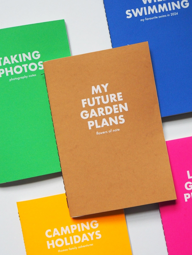 A group of colourful notebooks with personalised text. One notebooks says my future garden plans 