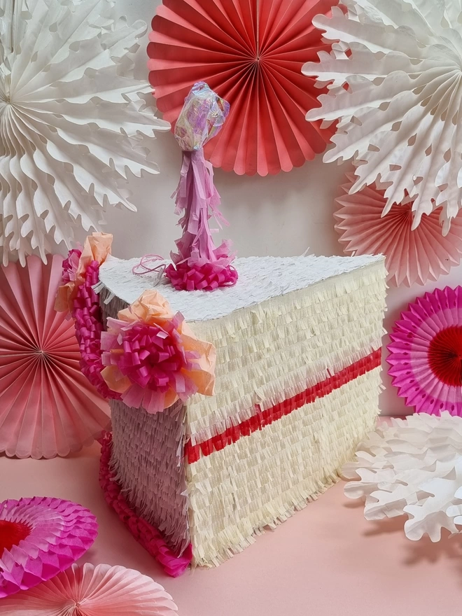 side view of cake pinata with pink candle and pink paper fans