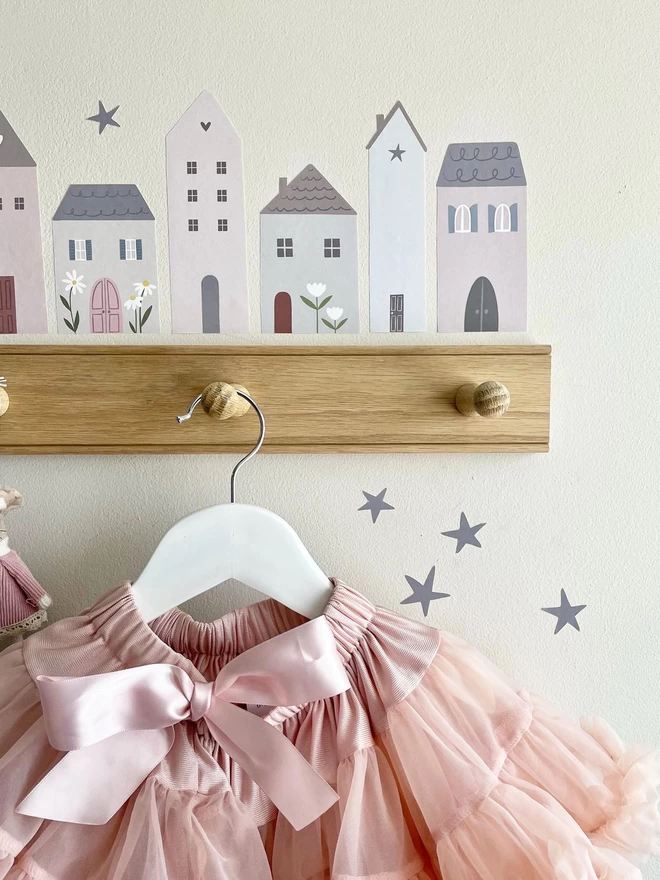 Girls bedroom with wall hooks, pink tutu and little village house stickers close up