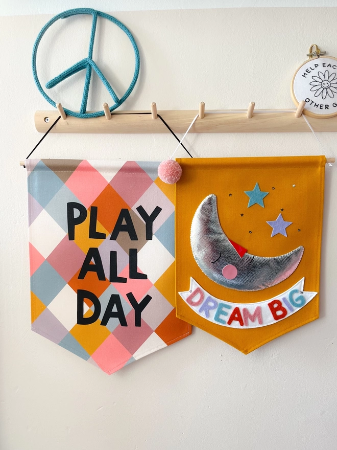 Play all day banner and dream big banner hanging from a wooden peg rail