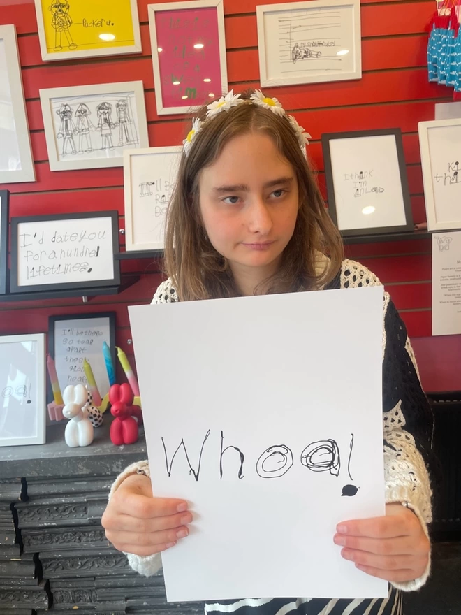 Piper a teenage, deaf, autistic artist from hackney is holding her art in her unique handwritten black font on a white background