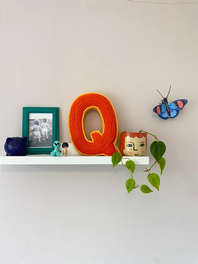 Crochet Q Cushion in Orange and Pale Orange, on a child's shelf