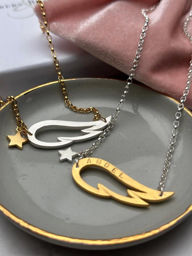 two necklaces. one a sterling silver chain with gold plated wing charm and small silver star. The other is a silver wing charm on a gold chain with gold mini star