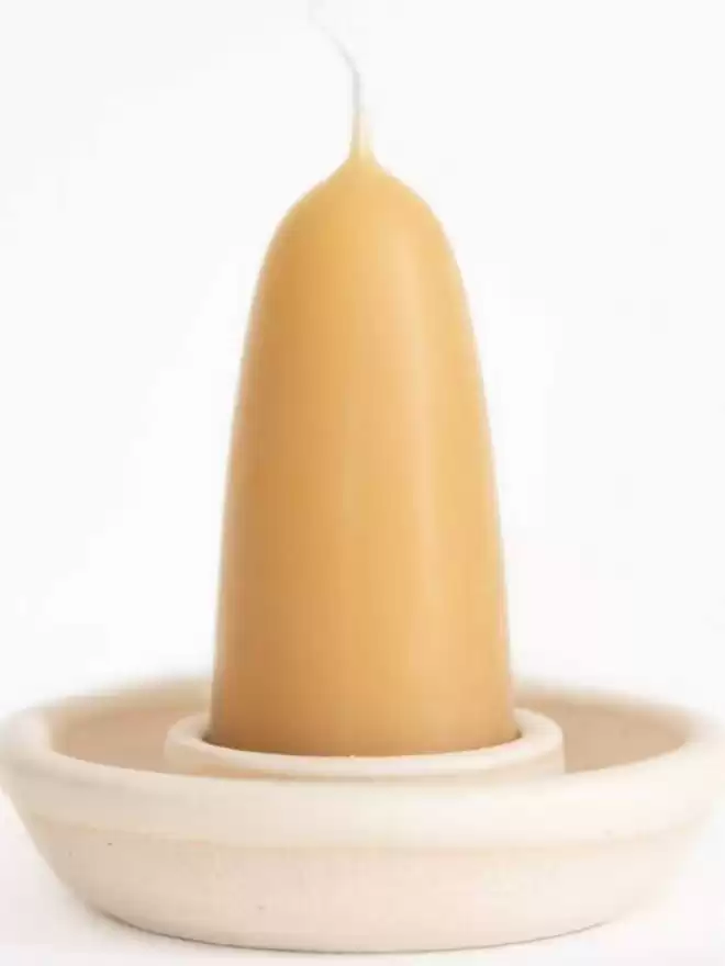 Close up of small stubby beeswax candle in a pearl white stoneware candle holder. White background