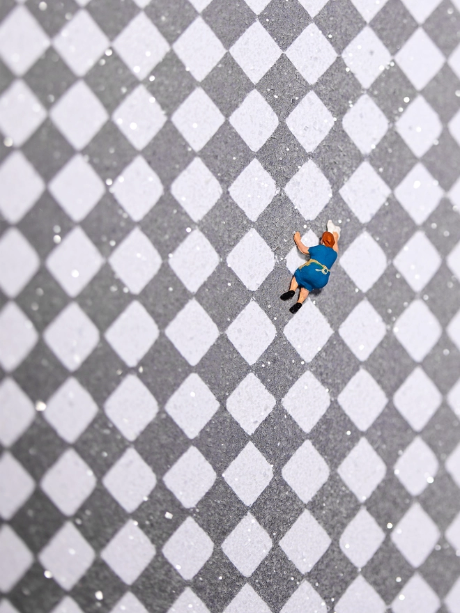 Miniature scene in an artbox showing a tiny cleaning lady washing a vast checkerboard floor 