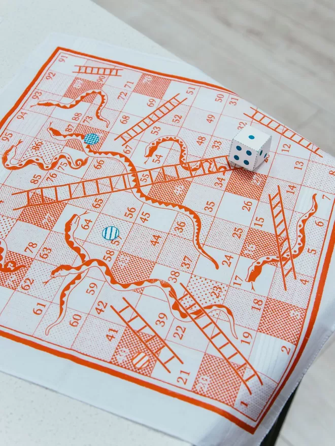 A Mr.PS Snakes and Ladders board game handkerchief with cut out dice and counters ready to play