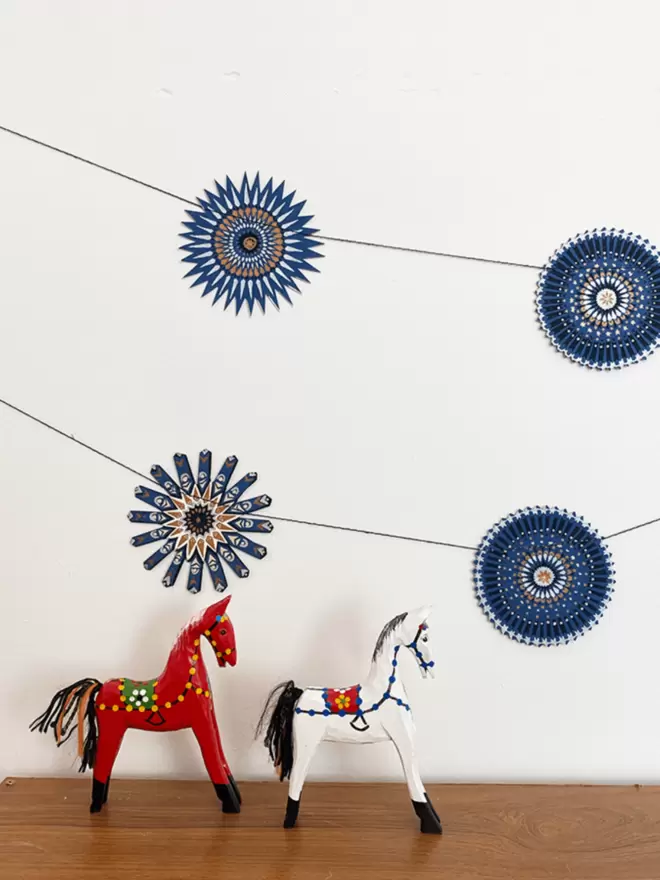 Paper garland hanging on white wall with wooden horses below 
