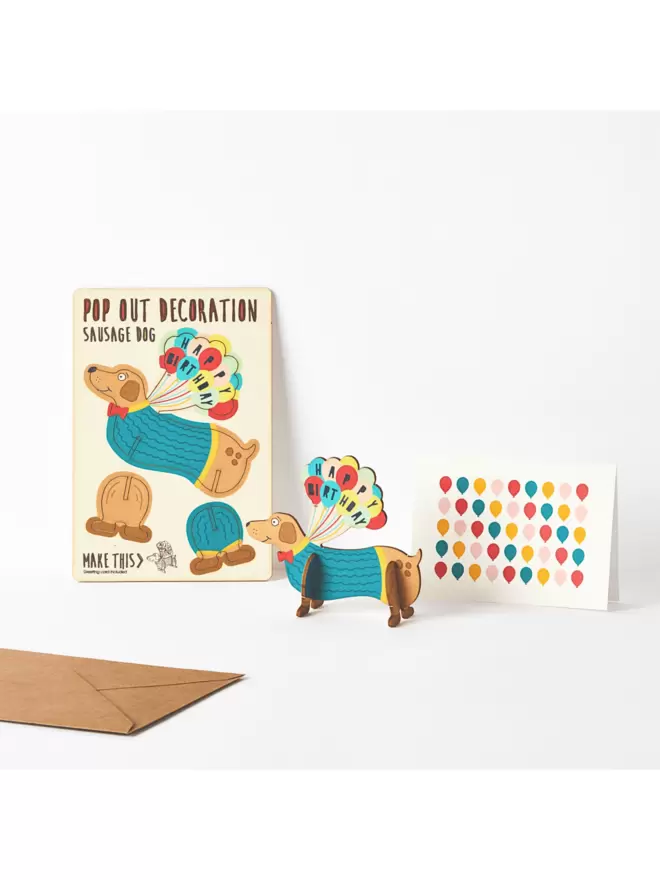 Sausage dog birthday decoration with coloured birthday balloon birthday card and brown kraft envelope on a white background