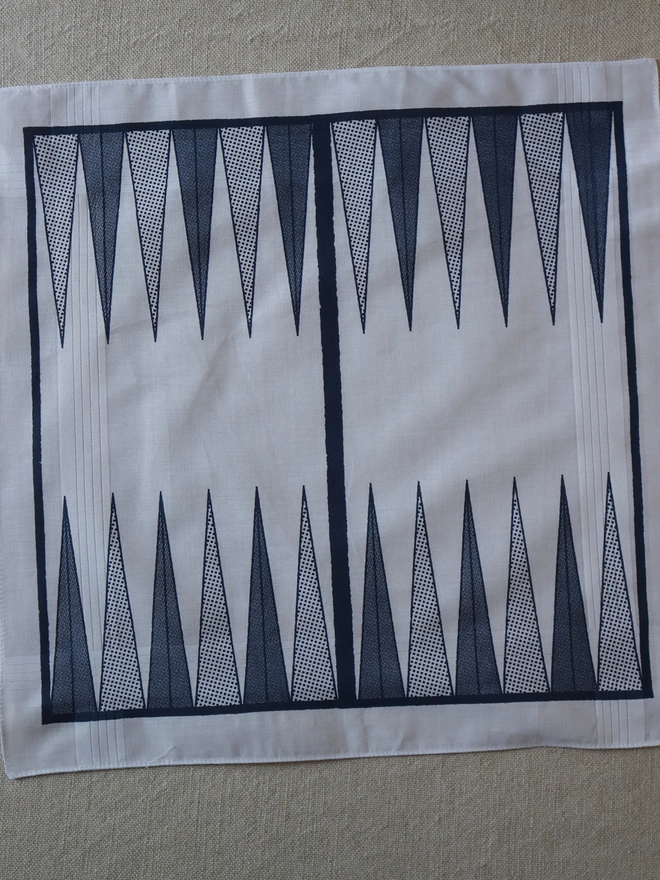 A Mr.PS Backgammon boardgame hankie printed in midnight blue laid flat on a linen tablecloth