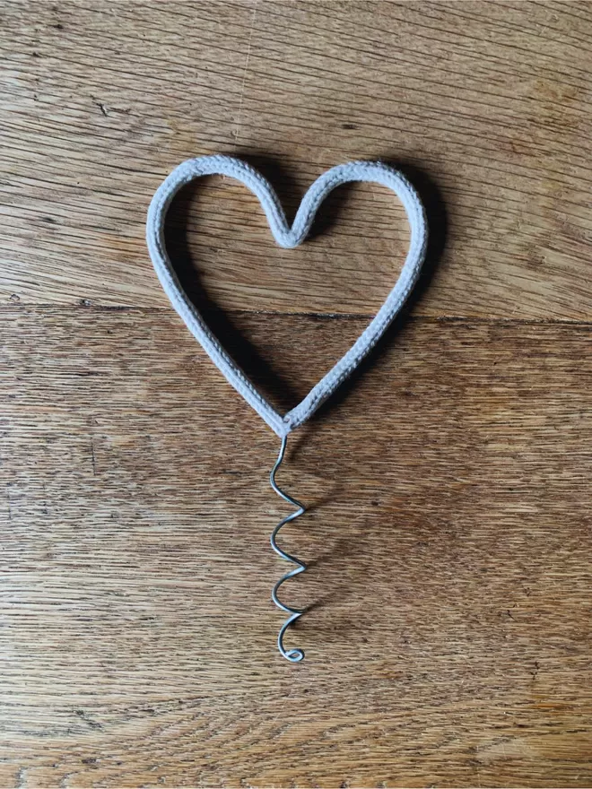 A white string wrapped wire heart shaped Christmas tree topper on an oak table