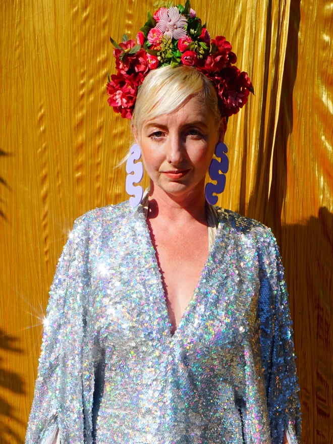 Silver Holographic Sequin V-neck Kaftan Gown seen on a woman standing in front of yellow fabric wearing a flower headdress.