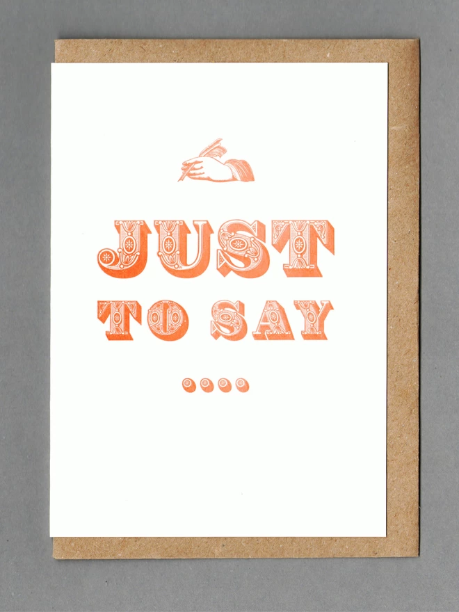 White card with an orange hand and orange text reading 'JUST TO SAY...' with a kraft envelope behind it
