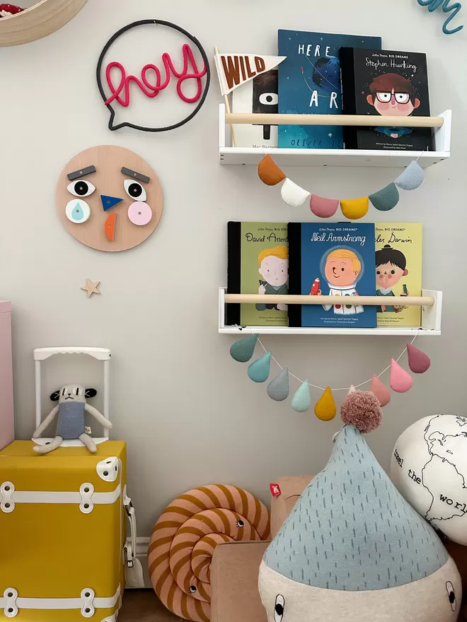"hey" speech bubble on the wall next to a bookshelf and above children's toys and decorations. 