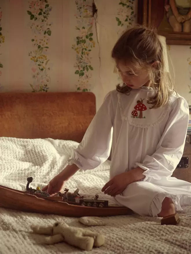 A girl on a bed in a nightie plays with a toy boat