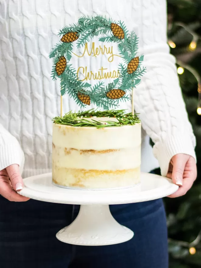 Model holds cake decorated with Christmas Wreath Cake Topper