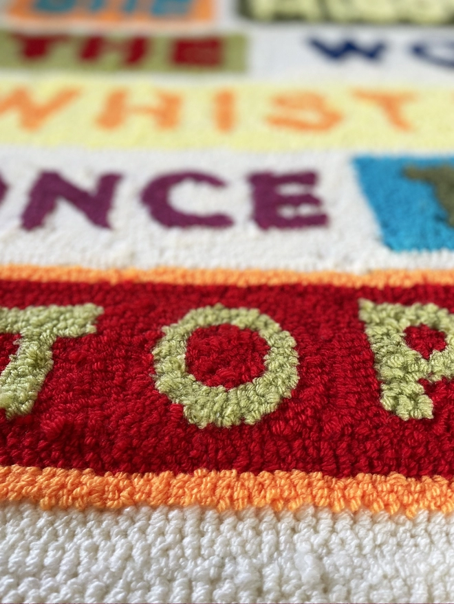 Close up of typographic punch needle textile art "She missed the wolf whistles once they stopped" in bright wool type with coloured block backgrounds