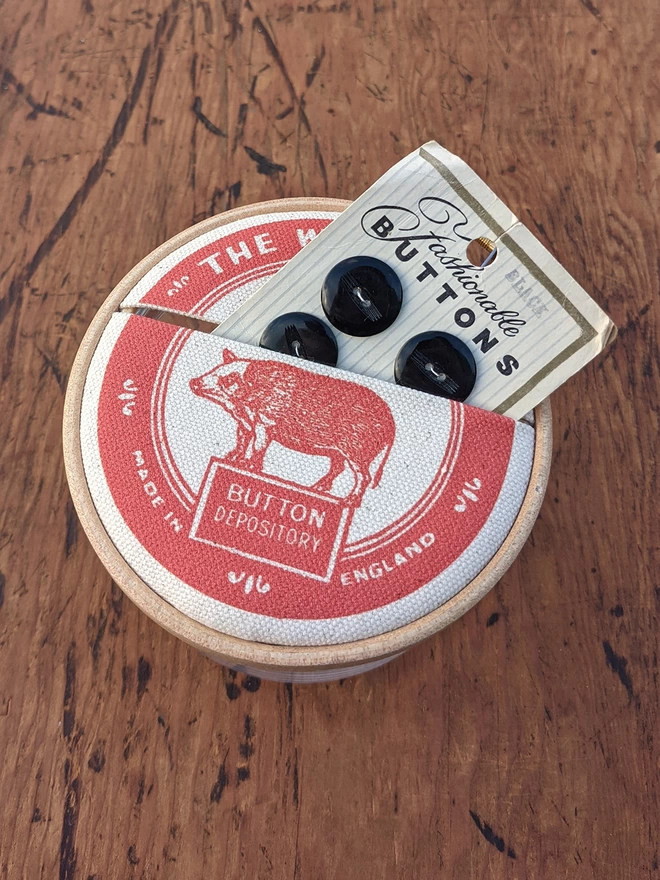 Packet of buttons sitting in red 'Wild Boar' Button Jar