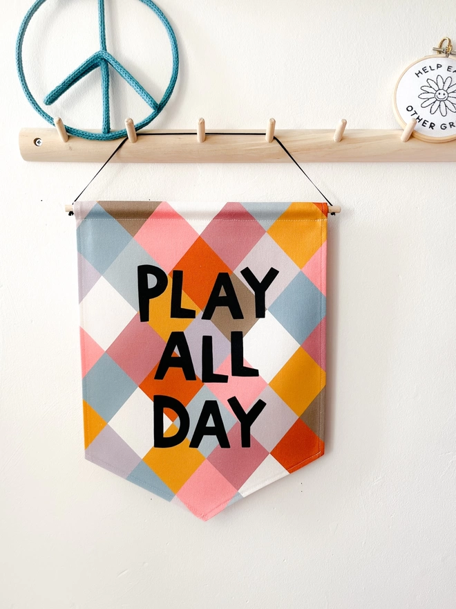 Printed sewn banner with the words play all day hanging from a wooden peg rail