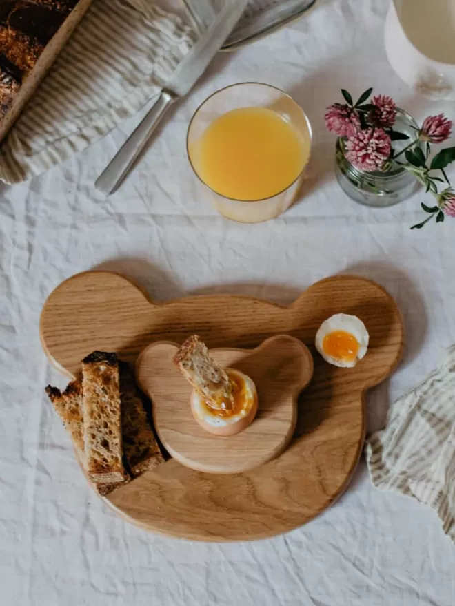 Wooden Egg Cup Bear resting on a Wooden Serving Board with dippy egg and soldiers
