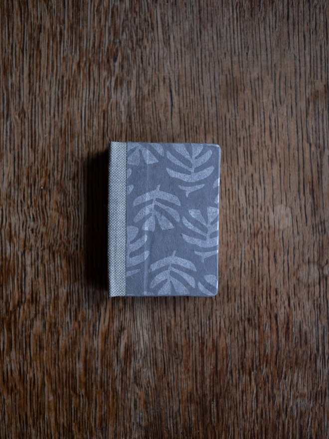 Miniature book with a grey cover with silver leaf pattern and beige cloth spine
