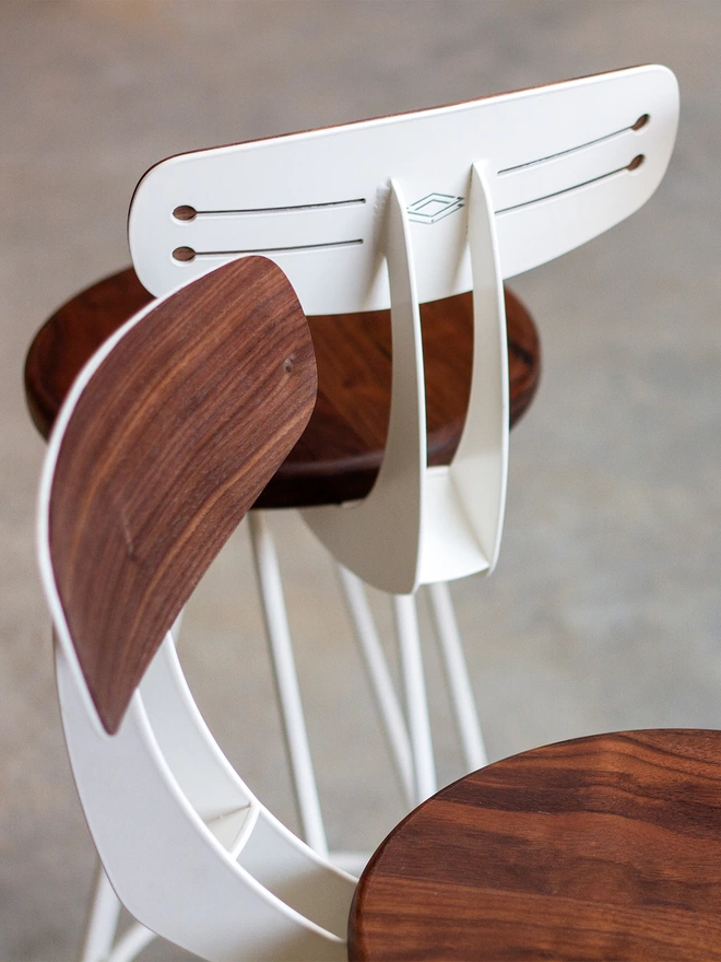 close up of two hairpin leg bar chairs with walnut seats and backs and white hair pin legs and steel work