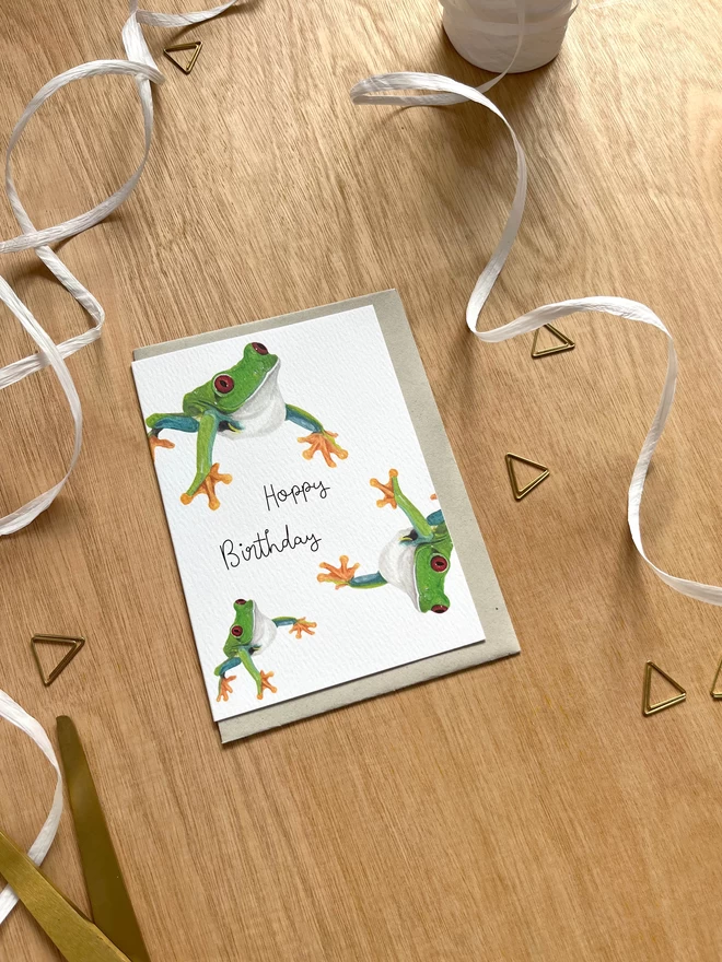 a greetings card featuring three green tree frogs with the phrase “hoppy birthday”