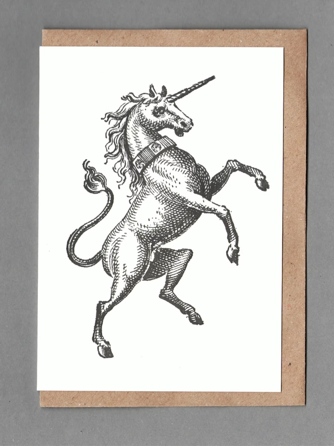 Black unicorn on white card with a brown envelope behind on a grey background