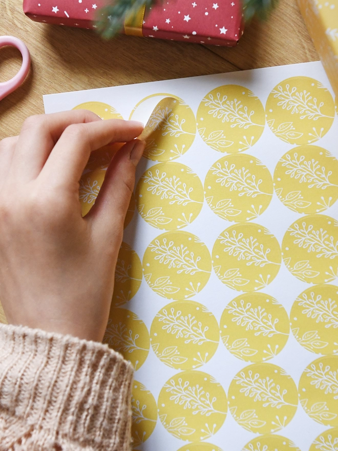 A hand is peeling a round sticker with a floral yellow design from a sheet of 35 stickers.