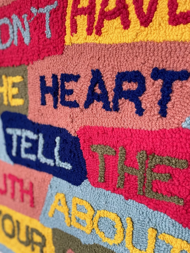 Close up of typographic textile art 'I didn't have the heart to tell the truth about your art' in primary colours on patchwork background