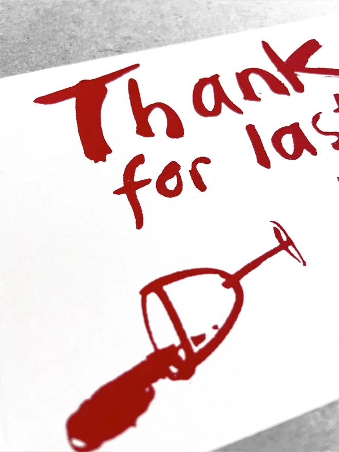 Close up of Thanks for Last night printed on white card with claret red ink. A knocked over wine glass is spilt across the bottom of the card.