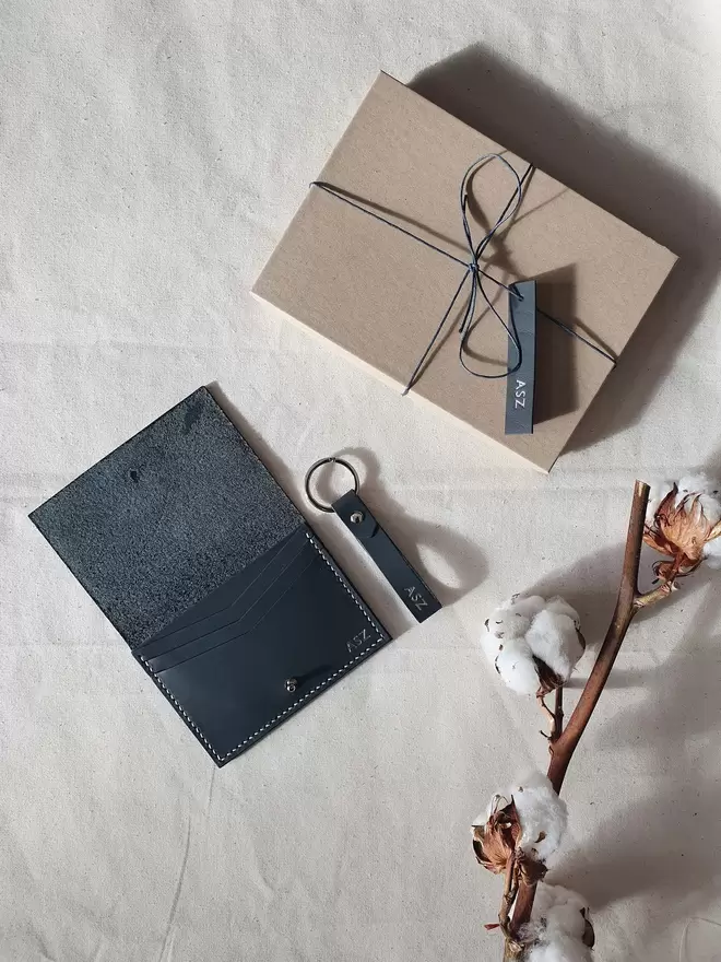 Grey wallet and keyring with cardboard gift box and matching grey leather tag on canvas background