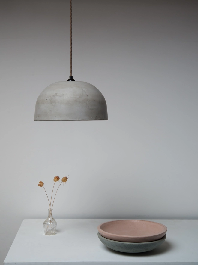 Large dome ceiling pendant lamp hanging above a table with two stacked concrete bowls