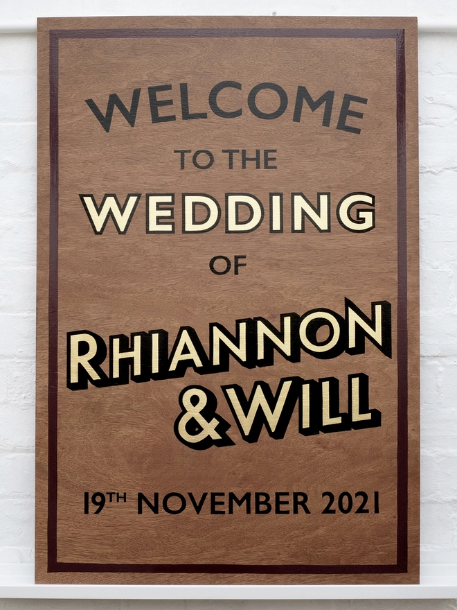 Hand painted welcome wedding sign with gold leaf, burgundy border with black outlined letters on dark wood. 