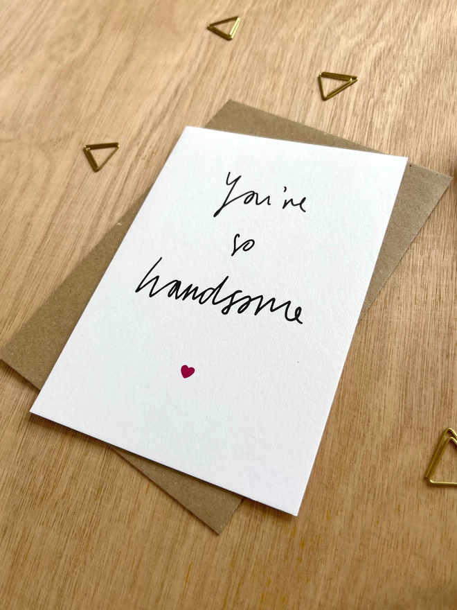a simple greetings card featuring hand drawn text saying “you’re so handsome” with a tiny pink heart
